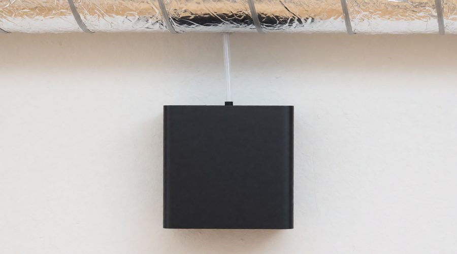 HVAC scent diffuser mounted on a wall with its tube feeding into a foil air duct